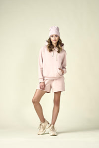 Woman in pale pink hoodie with matching shorts and matching pale pink beanie.