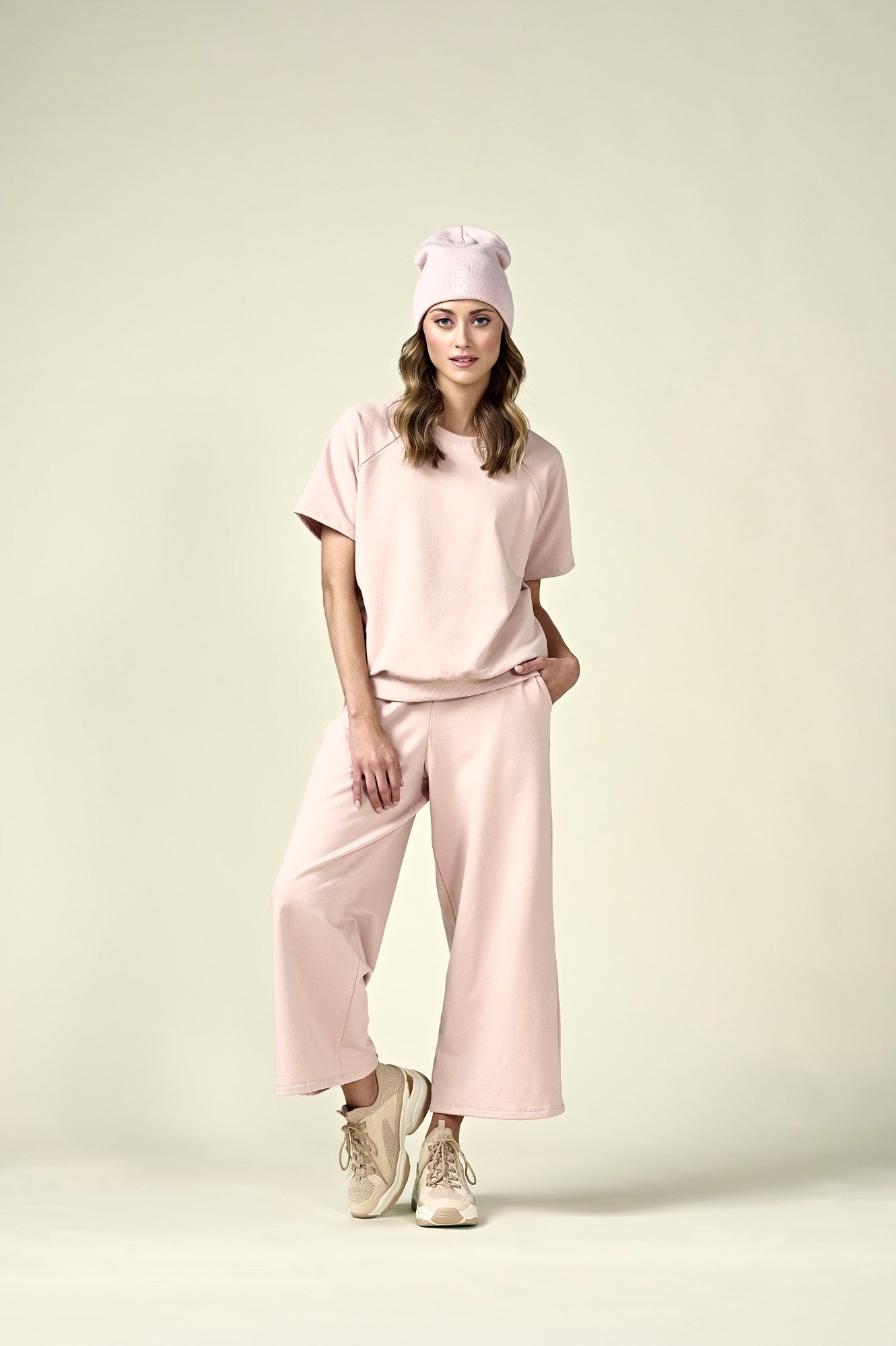 Woman in pale pink short sleeve sweatshirt, matching wide leg pants and matching pale pink beanie.