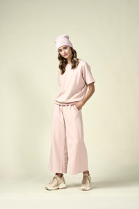 Woman in pale pink short sleeve sweatshirt, matching wide leg pants and matching pale pink beanie.