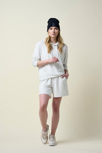 Woman wearing eggshell coloured shorts and hoodie with a black beanie.