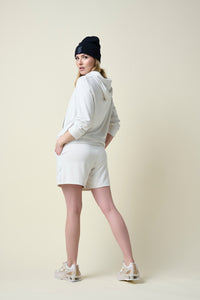 Back view of woman wearing eggshell coloured shorts and hoodie and black beanie.