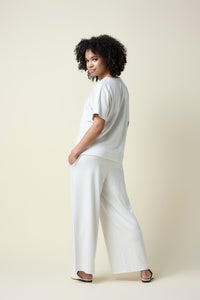 Back view of woman wearing eggshell wide leg pants and v-neck t-shirt and loafers.