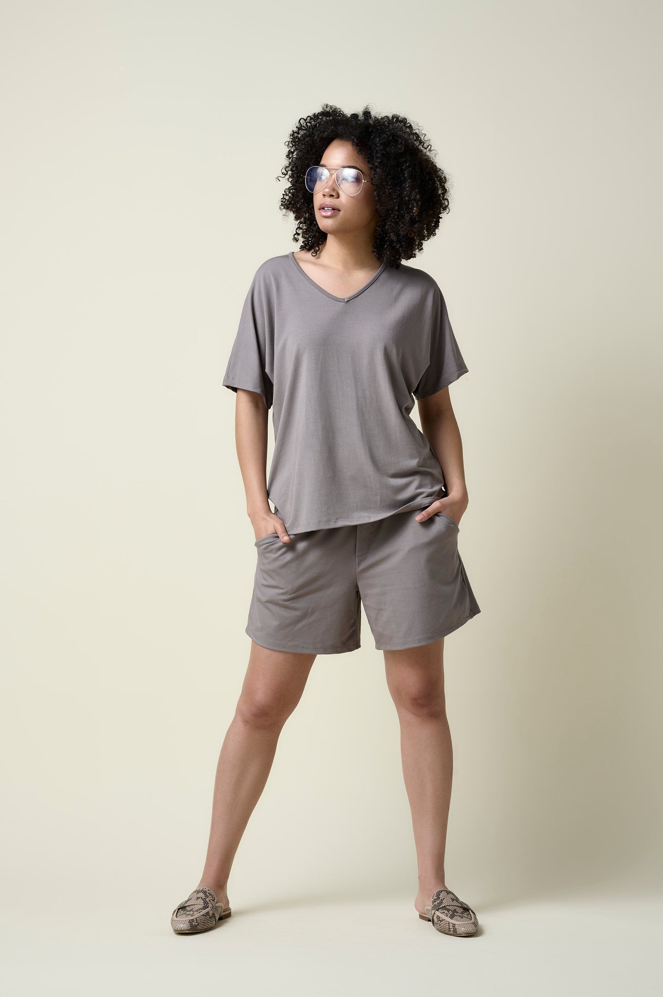 Woman wearing stone coloured shorts and matching v-neck t-shirt with loafers.